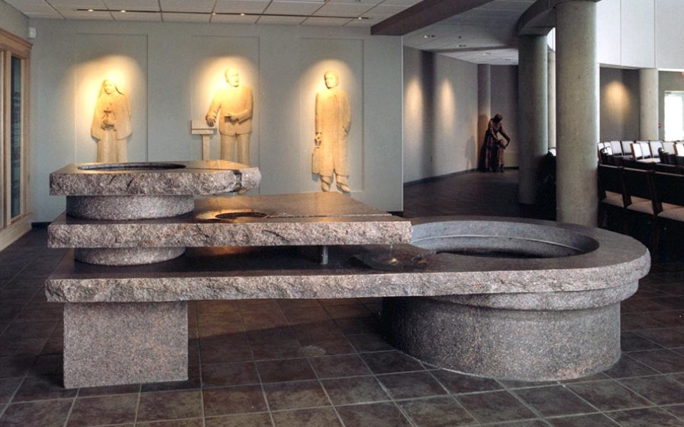 Just inside the main worship space is the three-tiered baptismal font made from eight tons of granite. Surrounding the font are six bas-relief modern witnesses to the baptismal ideals. On one side of the font are Mother Teresa of Calcutta (dedicated lover of the poor and neglected), Thomas Merton (Trappist monk and world-renowned writer), and Karl Rahner (influential Jesuit theologian). On the other side of the font are Martin Luther King, Jr. (civil rights leader), Therese of Lisieux (a Carmelite nun and Doctor of the Church), and Dorothy Day (lay peace and justice advocate and co-founder of the Catholic Worker Movement).